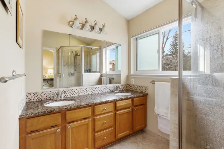 Bathroom with a shower stall, double vanity, backsplash, and light tile patterned floors