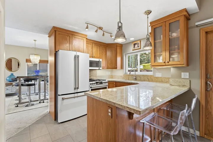 Kitchen featuring a kitchen bar, stainless steel appliances, light stone countertops, wood finish cabinetry, and a peninsula