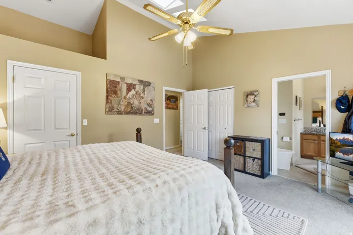 Bedroom with vaulted ceiling, carpet flooring, a skylight, connected bathroom, and a ceiling fan