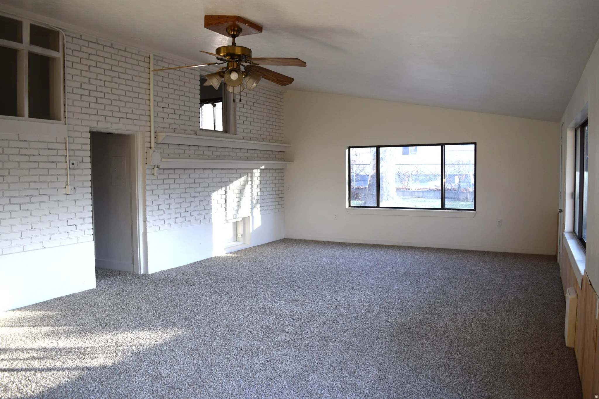 Carpeted empty room with brick wall, lofted ceiling, and a ceiling fan
