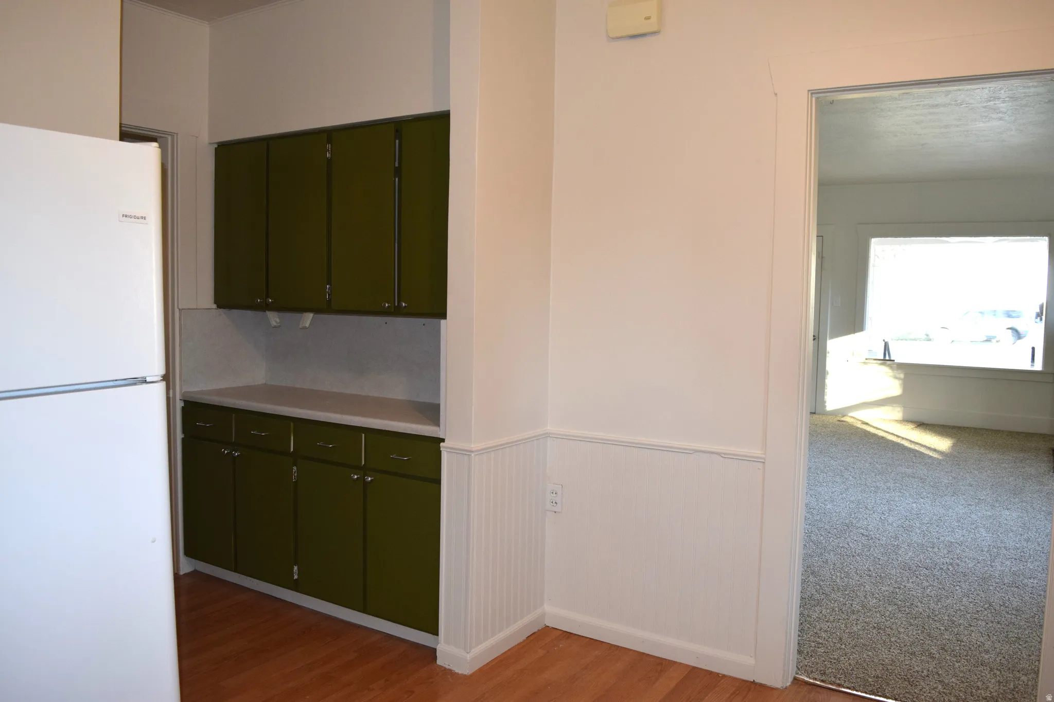 Kitchen featuring freestanding refrigerator, light countertops, green cabinets, light wood-style floors, and a wainscoted wall