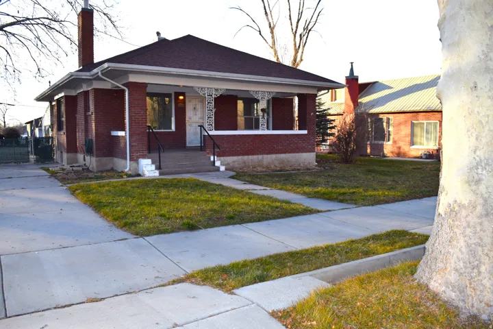 Bungalow-style home with covered porch, brick siding, a front yard, and a chimney