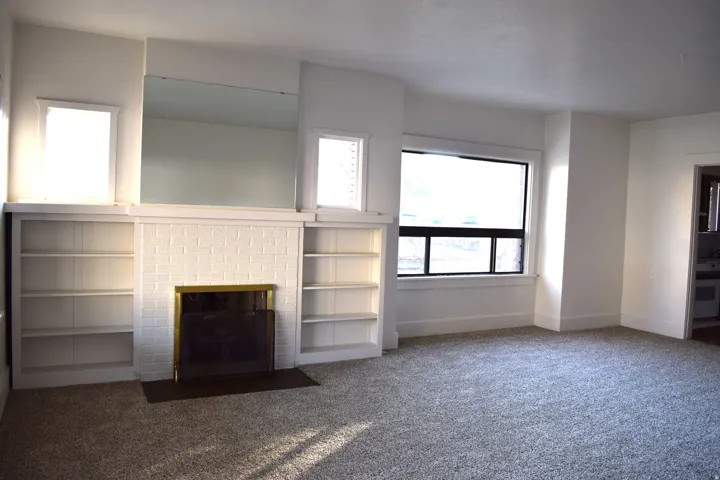 Unfurnished living room with carpet flooring and a brick fireplace