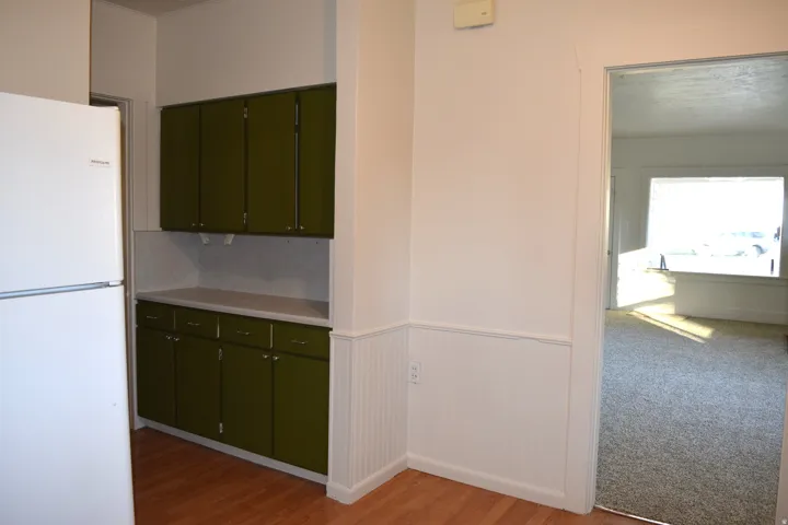 Kitchen featuring freestanding refrigerator, light countertops, green cabinets, light wood-style floors, and a wainscoted wall