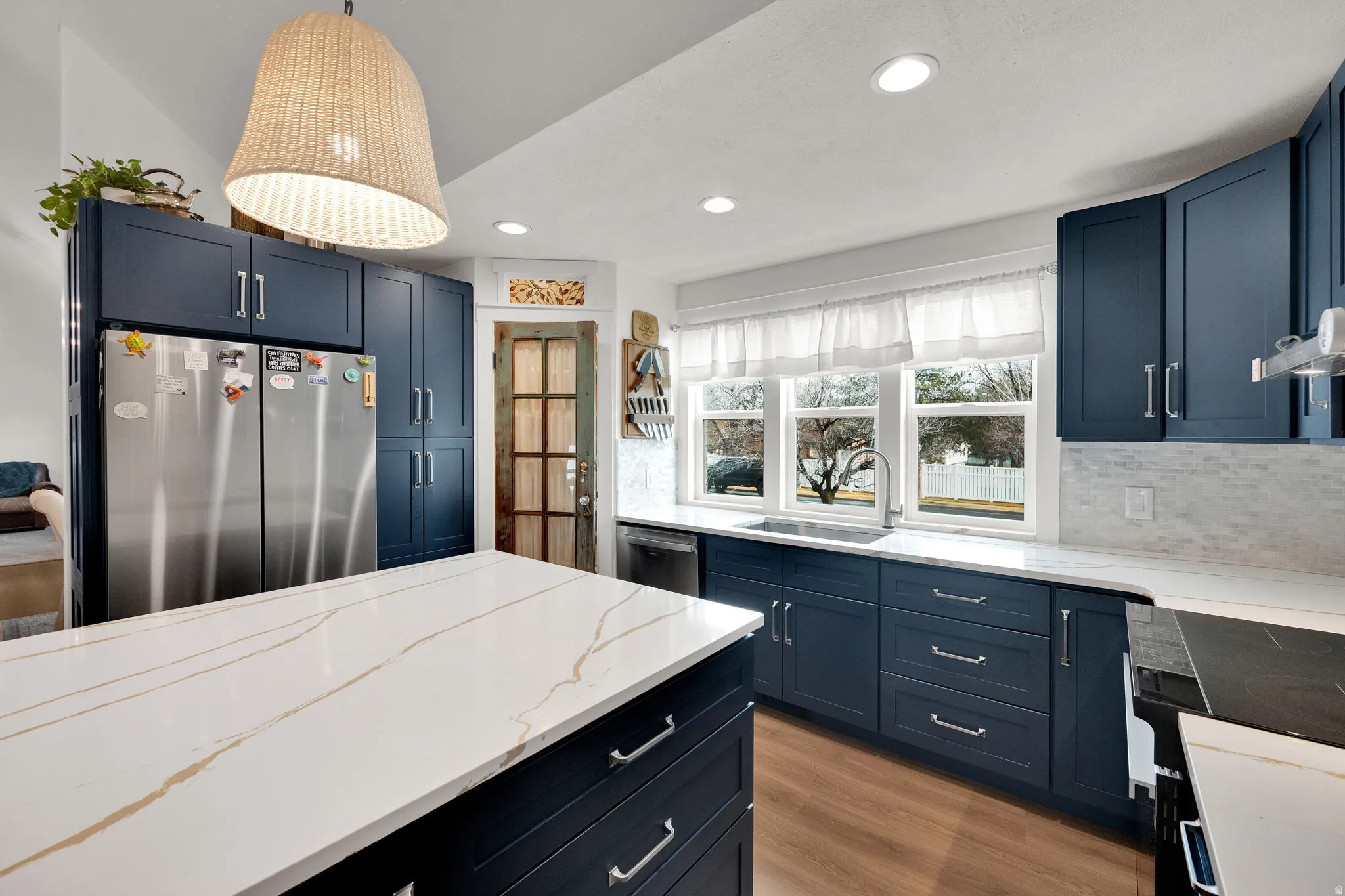 Kitchen featuring stainless steel appliances, blue cabinetry, hanging light fixtures, and light wood-style floors