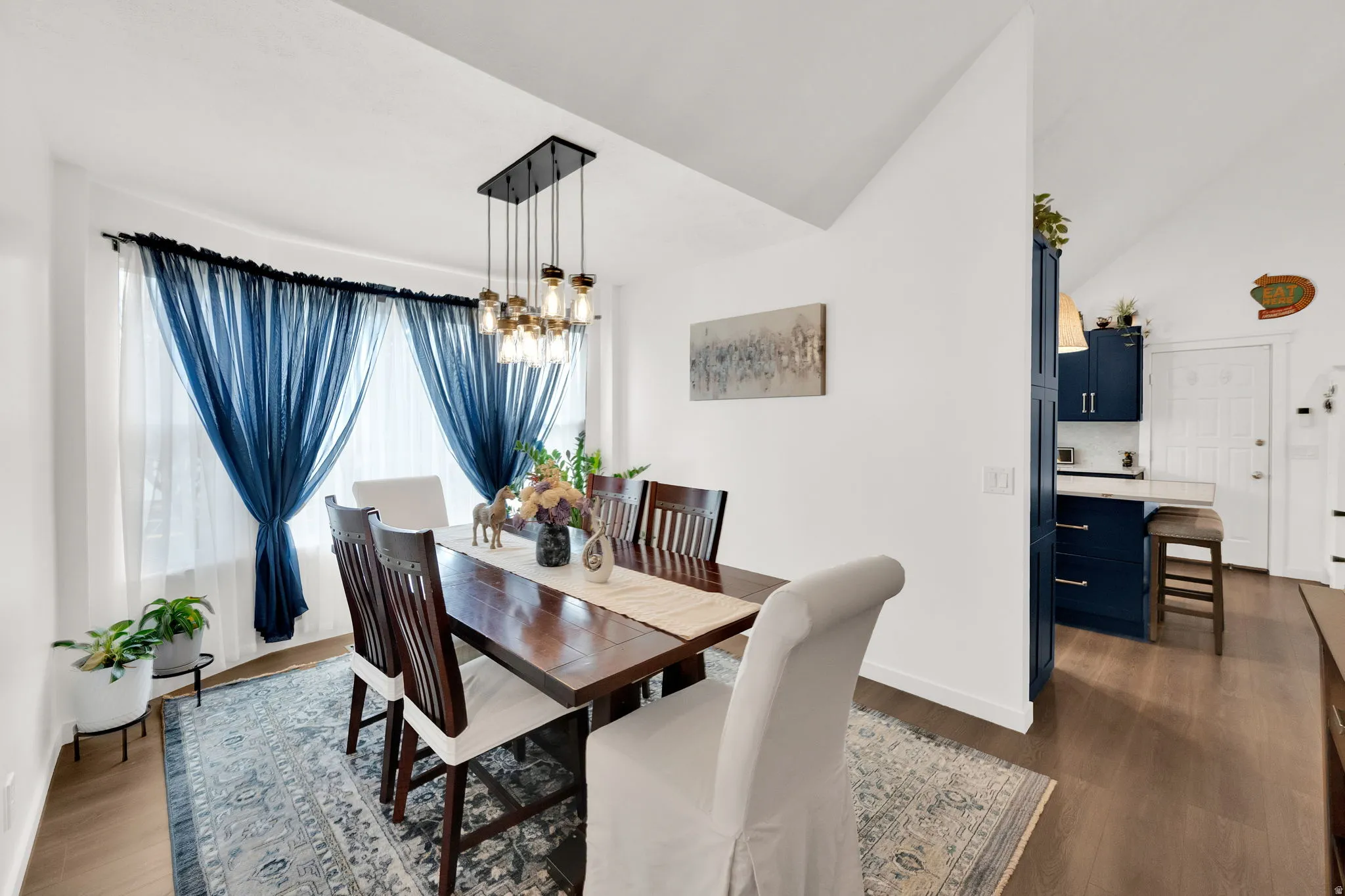 Dining room with dark wood-style flooring, lofted ceiling, and suspended lighting