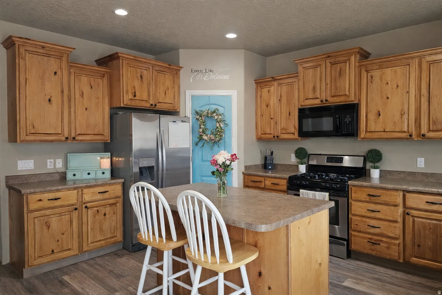 Kitchen with stainless steel appliances, a breakfast bar, wood finish cabinetry, a center island, and a textured ceiling