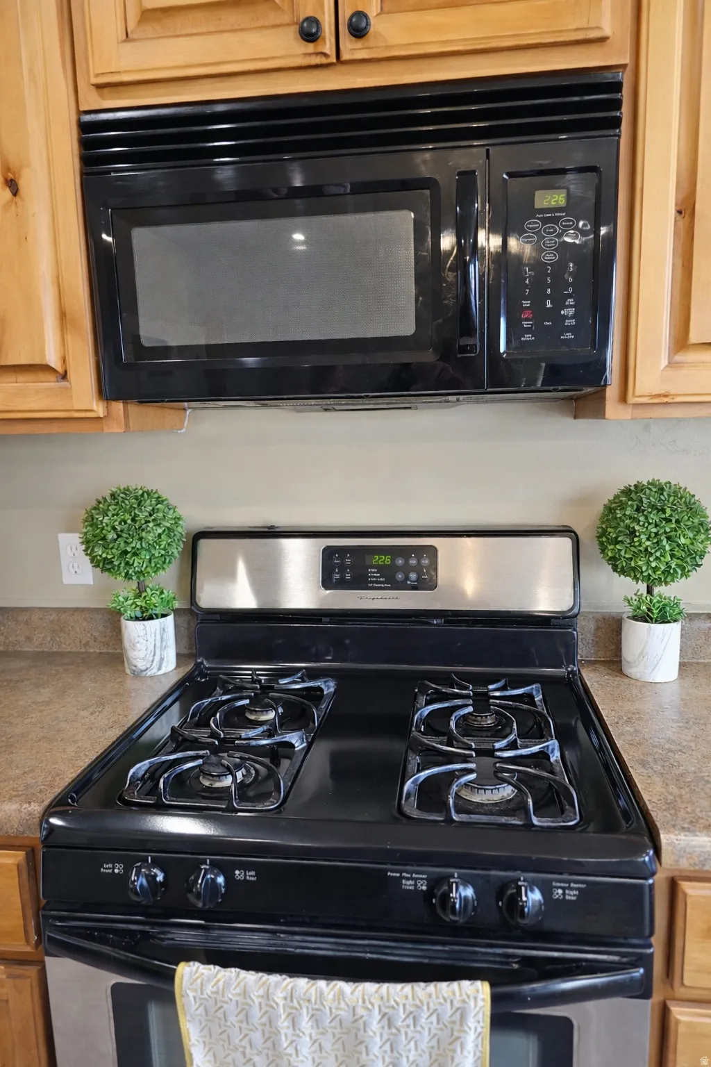 Kitchen view of black microwave, stainless steel gas stove, light countertops, and light wood finish cabinets
