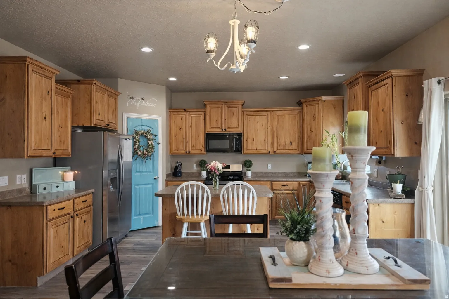Kitchen featuring suspended lighting, a kitchen island, stainless steel appliances, dark wood-style flooring, and wood finish cabinets