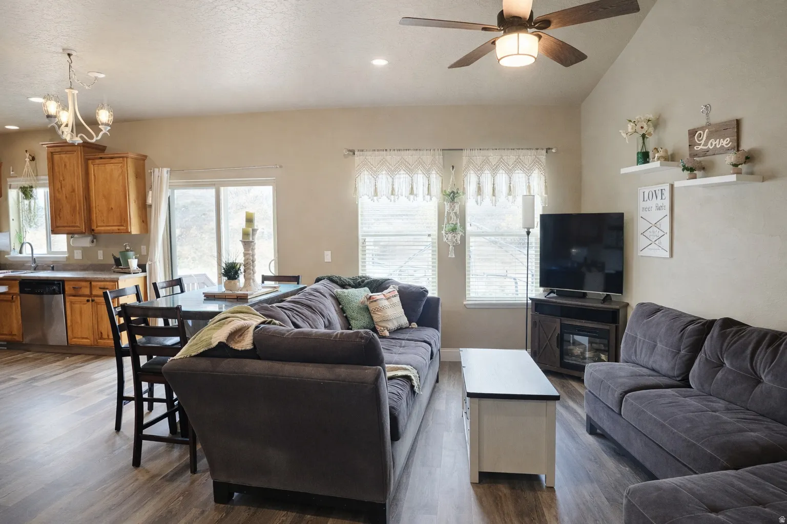 Living area featuring a ceiling fan, dark wood-style floors, healthy amount of natural light, suspended lighting, and lofted ceiling
