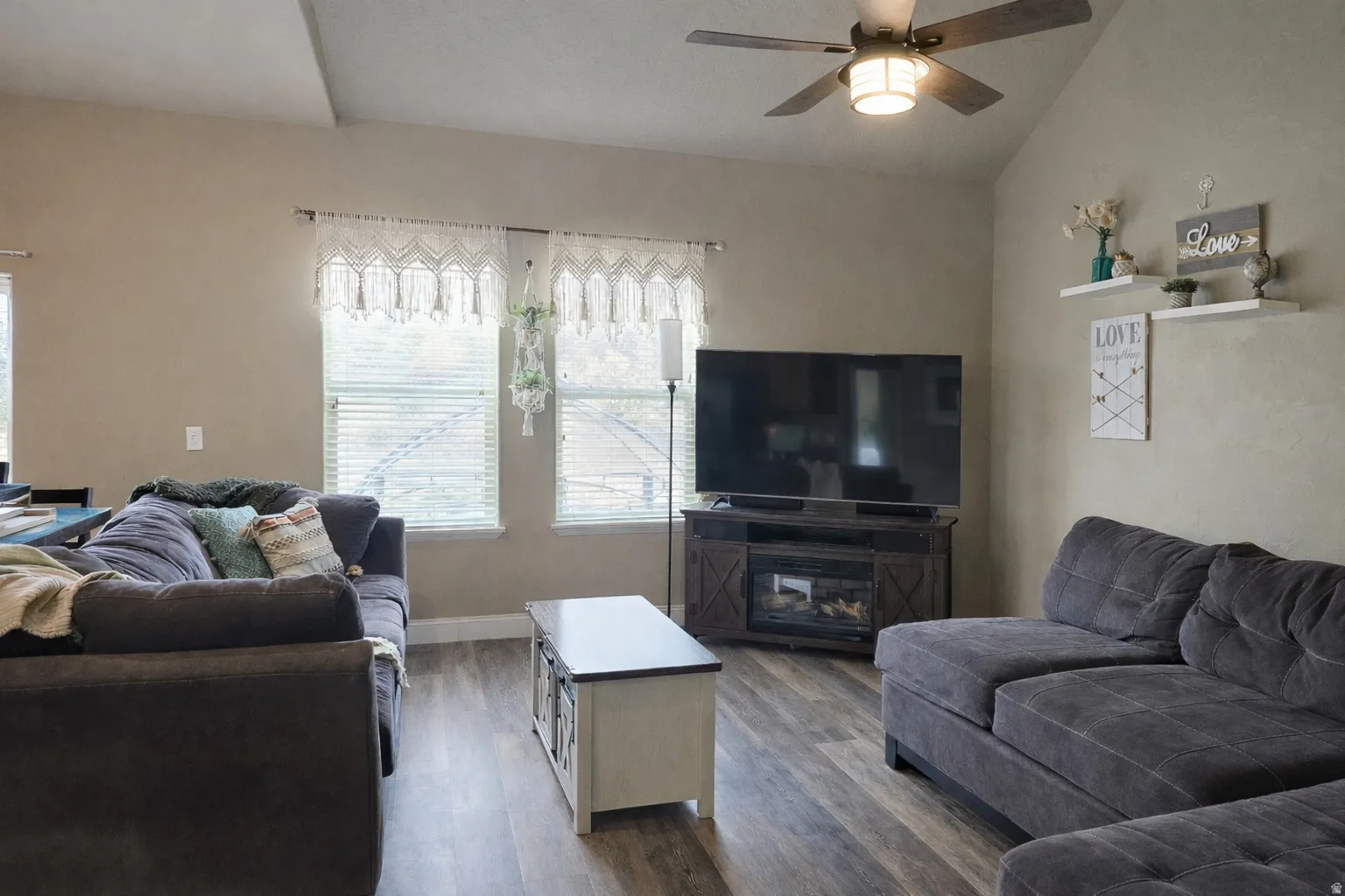 Living room with a ceiling fan, vaulted ceiling, and dark wood-type flooring