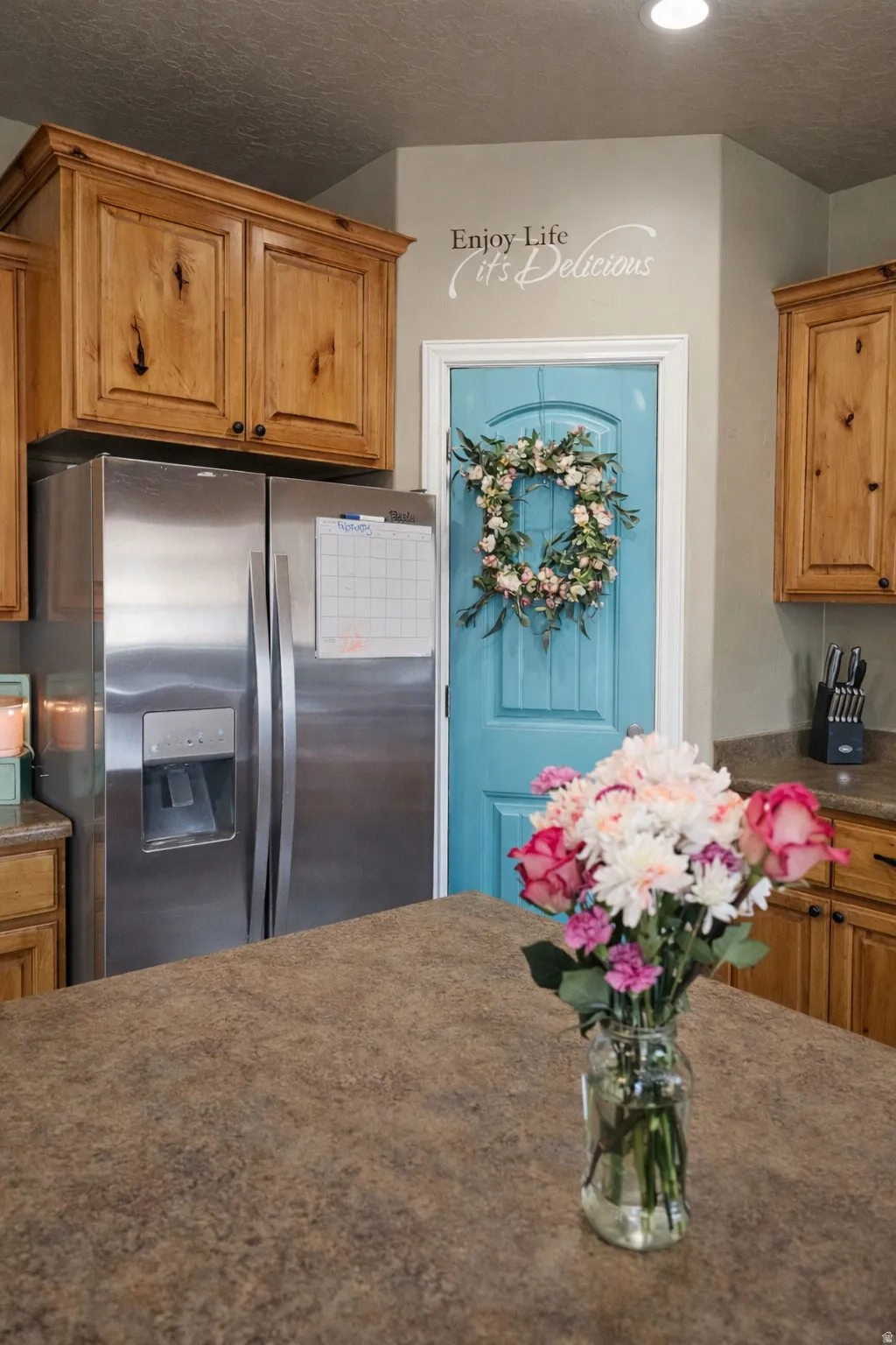 Kitchen featuring wood finish cabinetry, stainless steel refrigerator with ice dispenser, dark stone counters, and a textured ceiling