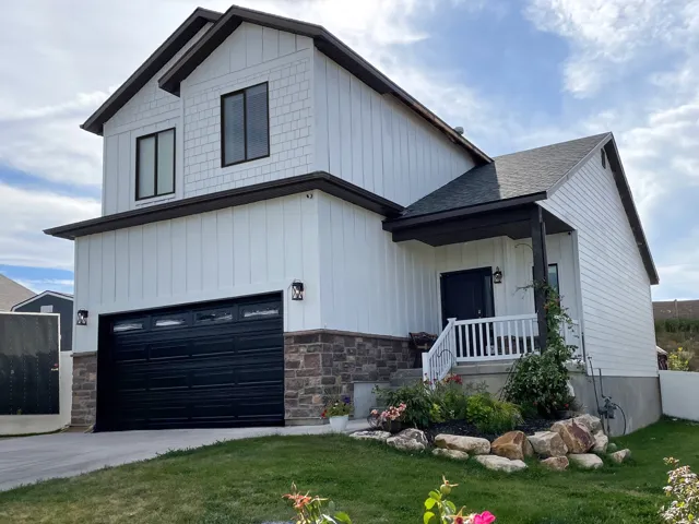 Modern inspired farmhouse with covered porch, stone siding, a garage, board and batten siding, and a shingled roof