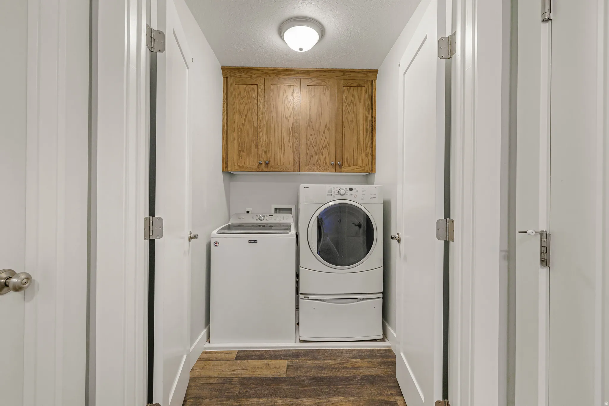 Laundry room with dark wood-style floors, cabinet space, washing machine and dryer, and a textured ceiling