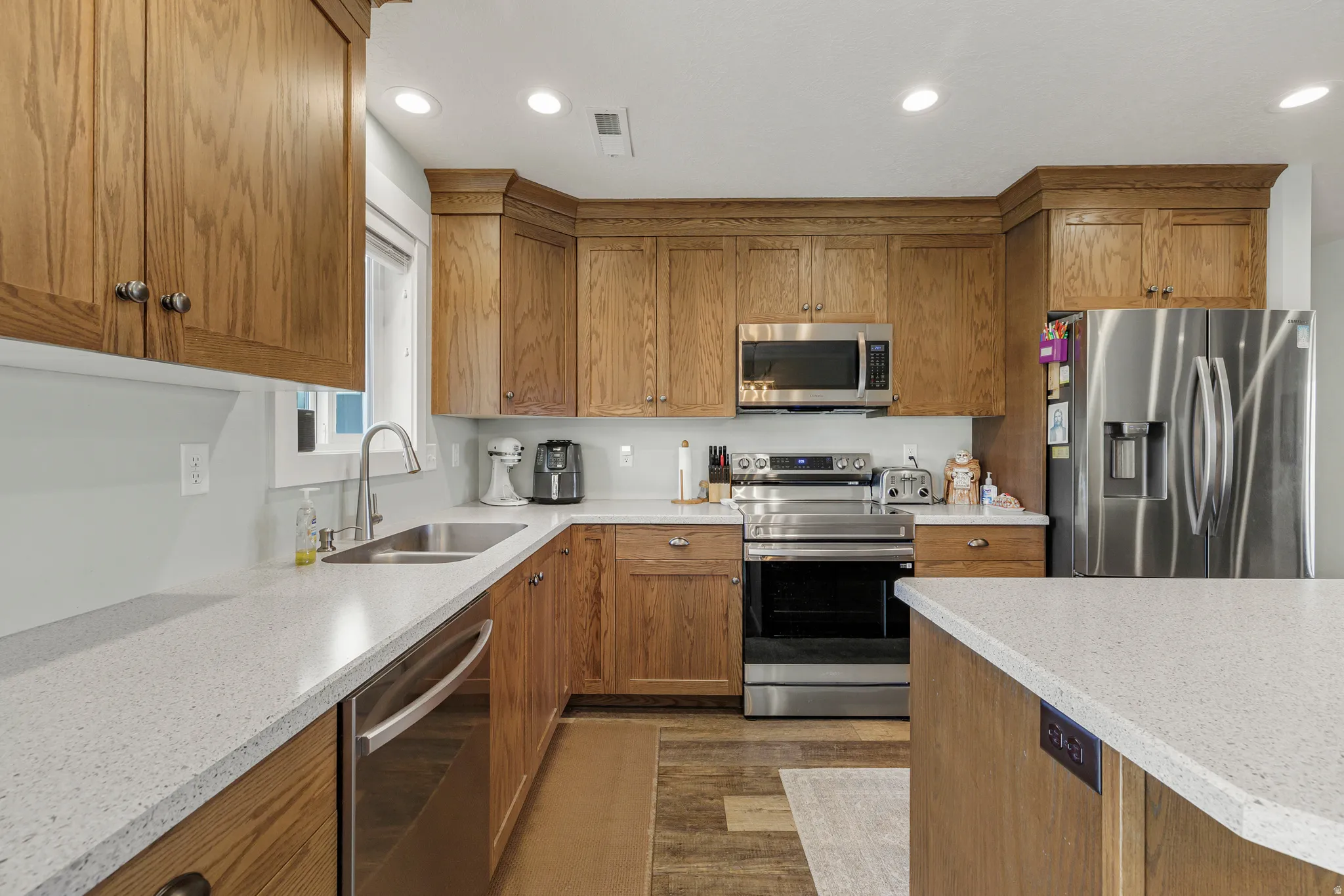 Kitchen featuring wood finish cabinets, stainless steel appliances, light stone counters, recessed lighting, and dark wood finished floors