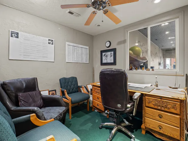 Office with a textured wall, dark colored carpet, and a ceiling fan