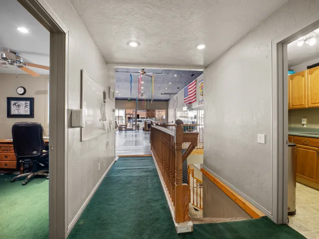 Hallway with a textured wall, dark carpet, a textured ceiling, a desk, and recessed lighting