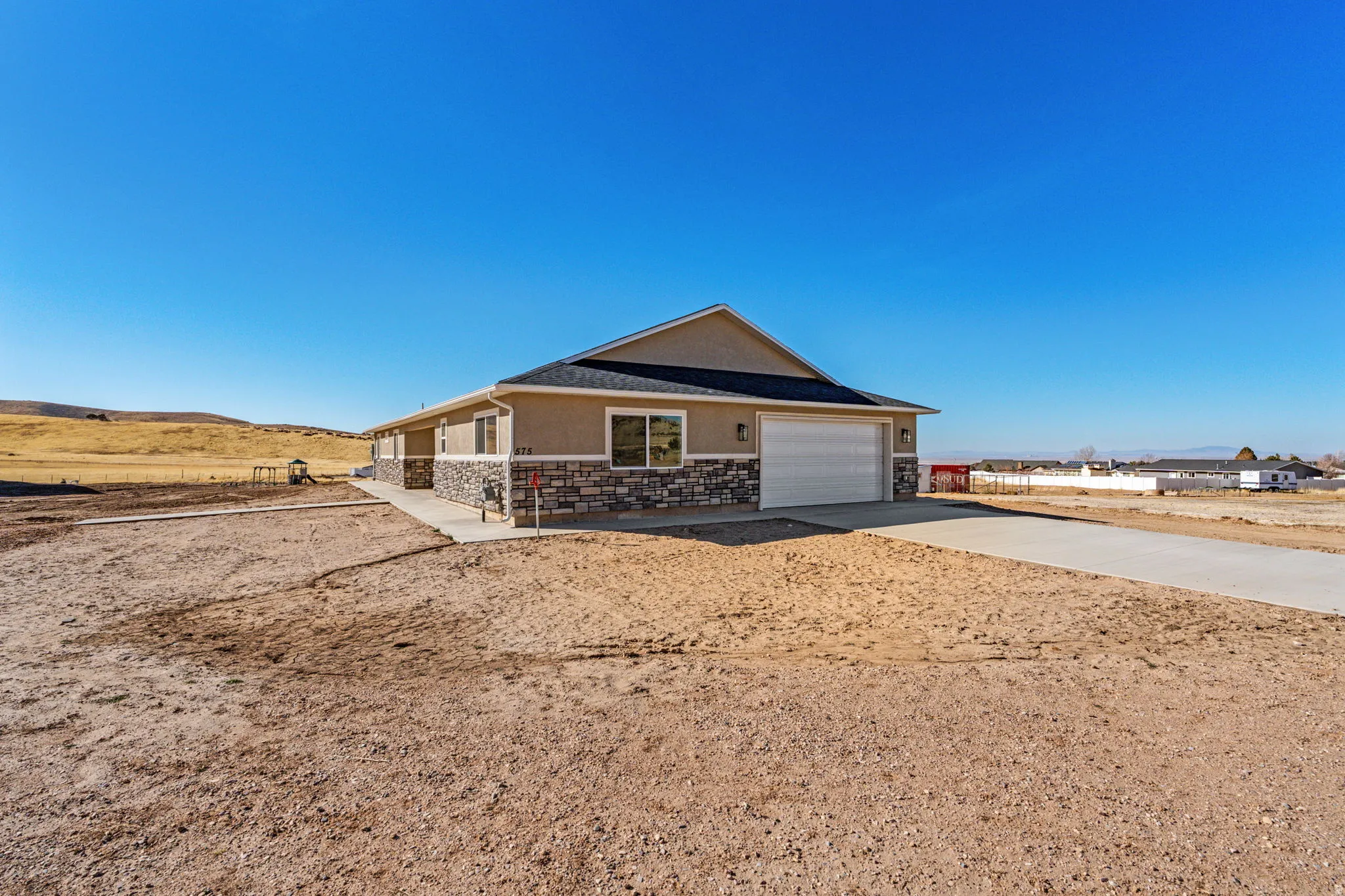 Ranch-style home with driveway, stucco siding, stone siding, and a garage