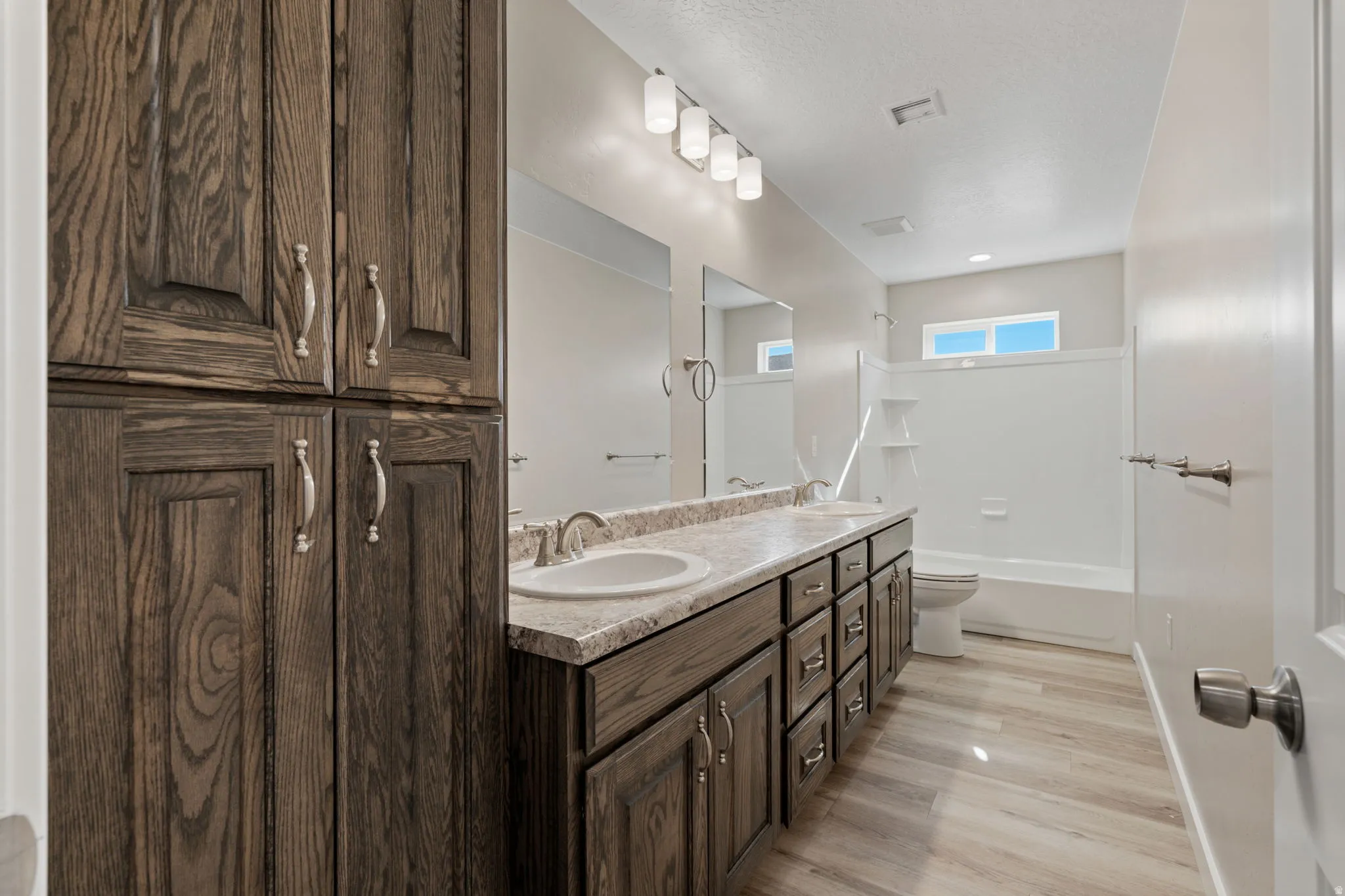 Bathroom with double vanity, bathtub / shower combination, light wood-style floors, and a textured ceiling