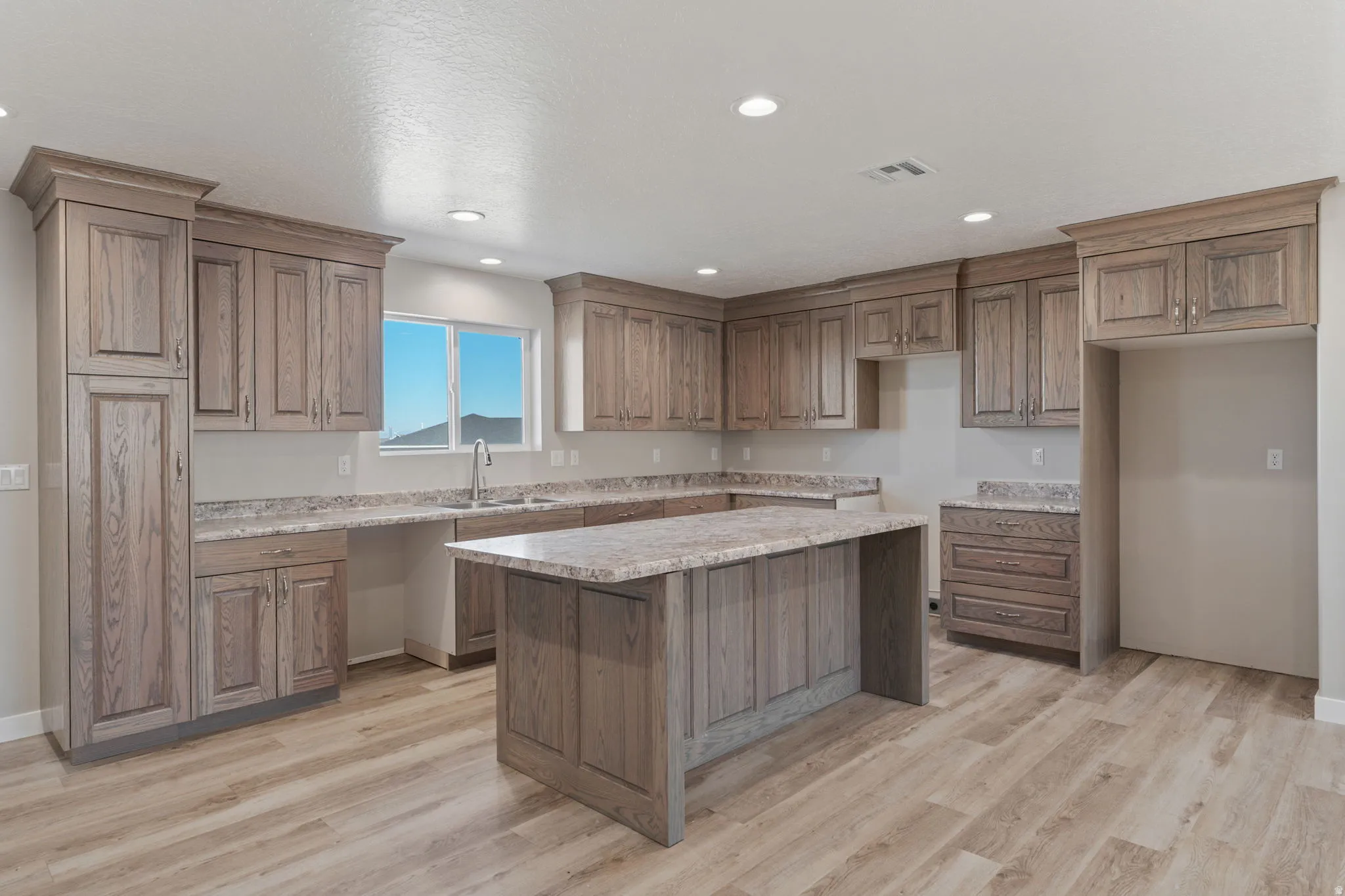 Kitchen featuring wood finish cabinets, light wood-style flooring, a center island, light stone counters, and recessed lighting