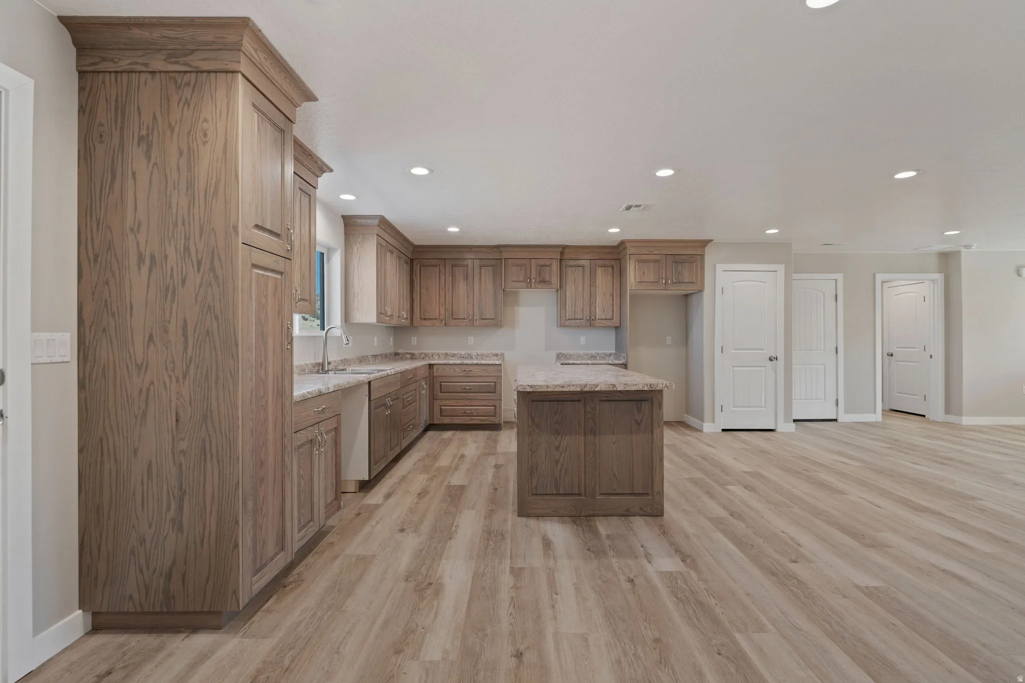 Kitchen with wood finish cabinets, a kitchen island, light wood-type flooring, recessed lighting, and light stone counters