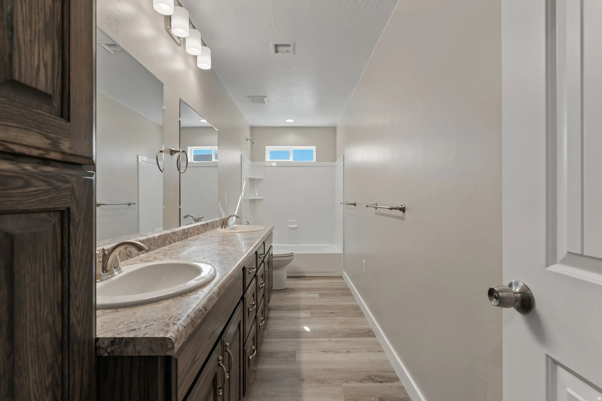 Bathroom with double vanity, shower / bath combination, light wood-type flooring, and a textured ceiling
