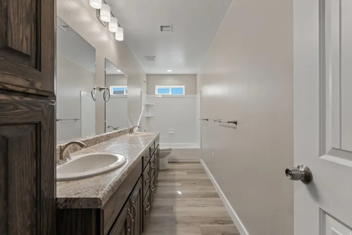 Bathroom with double vanity, shower / bath combination, light wood-type flooring, and a textured ceiling