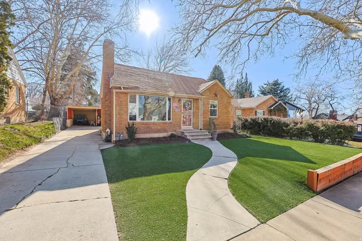 Bungalow-style home featuring brick siding, a front yard, a chimney, driveway, and roof with shingles