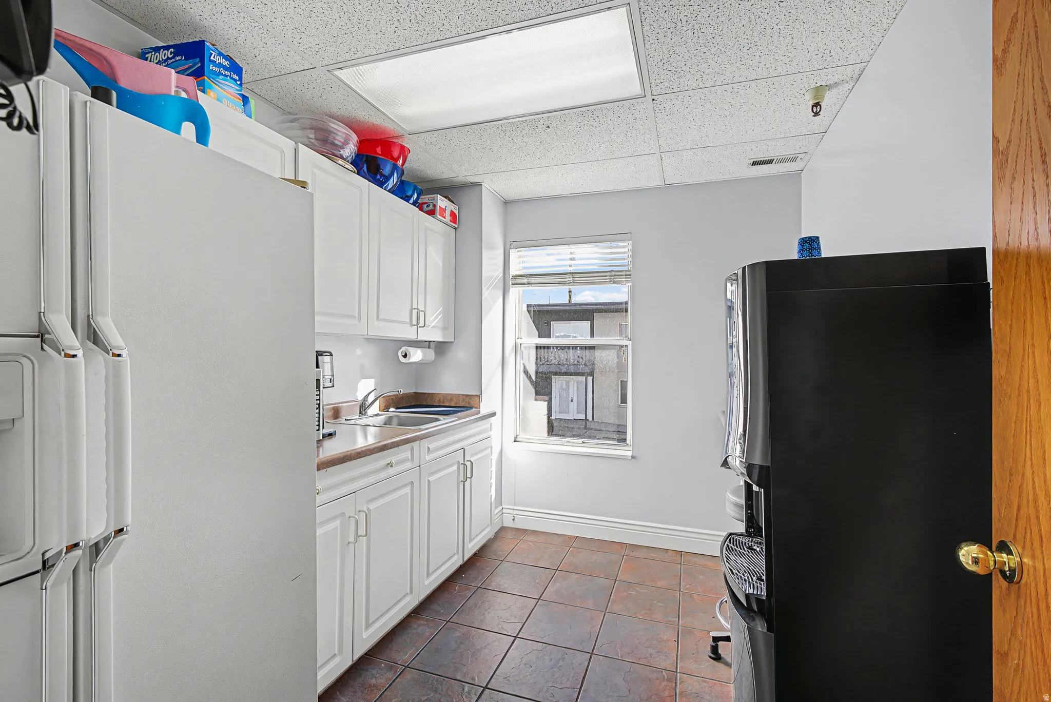 Kitchen with white fridge with ice dispenser, white cabinetry, freestanding refrigerator, a drop ceiling, and light countertops