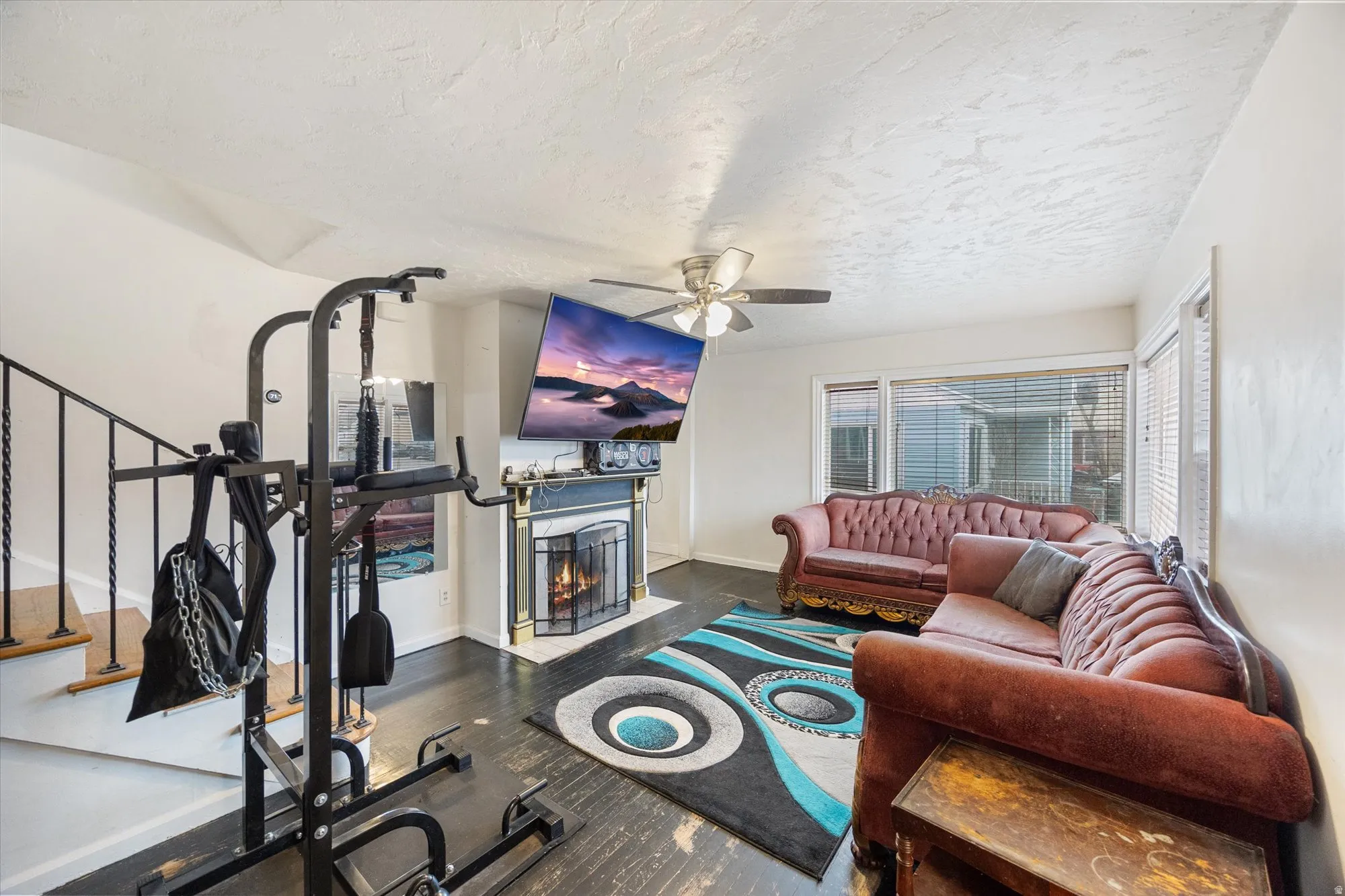 Workout area featuring a fireplace with flush hearth, a ceiling fan, a textured ceiling, and dark wood-type flooring
