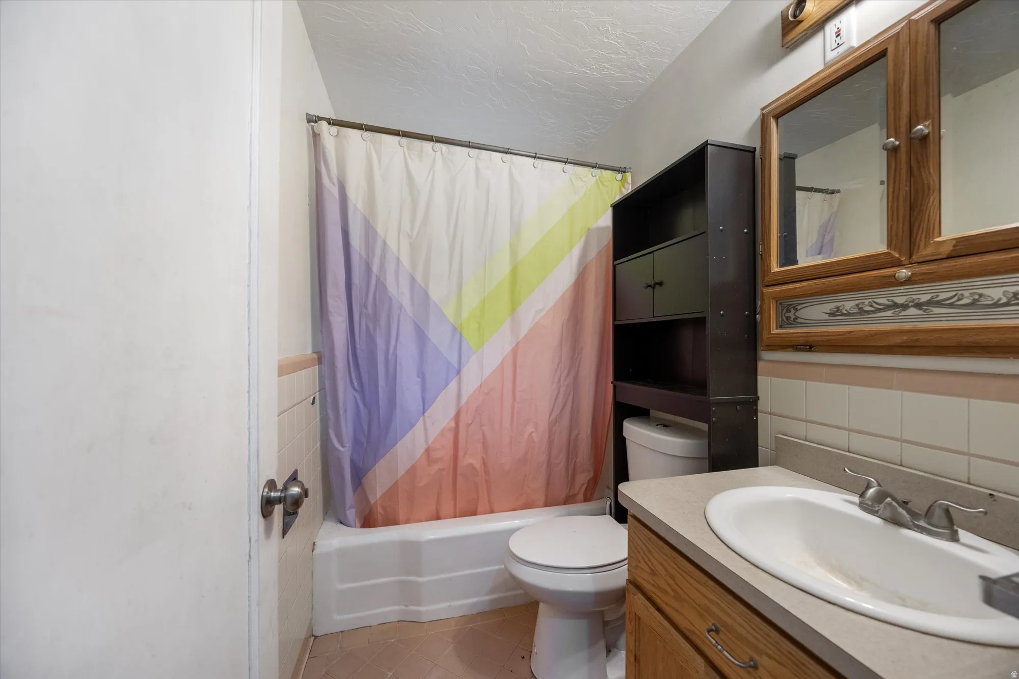 Bathroom featuring vanity, shower / tub combo, a textured ceiling, tile walls, and wainscoting
