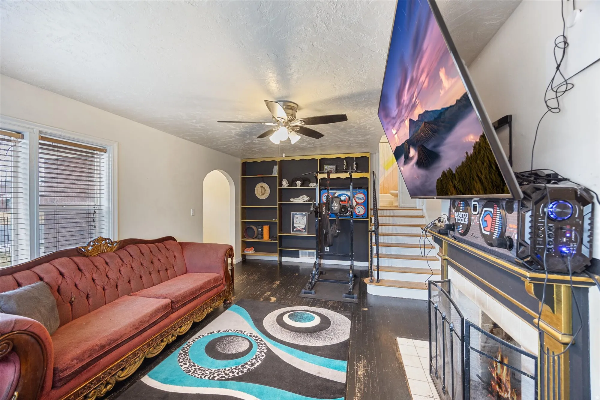 Living area with dark wood finished floors, arched walkways, a textured ceiling, ceiling fan, and a tiled fireplace