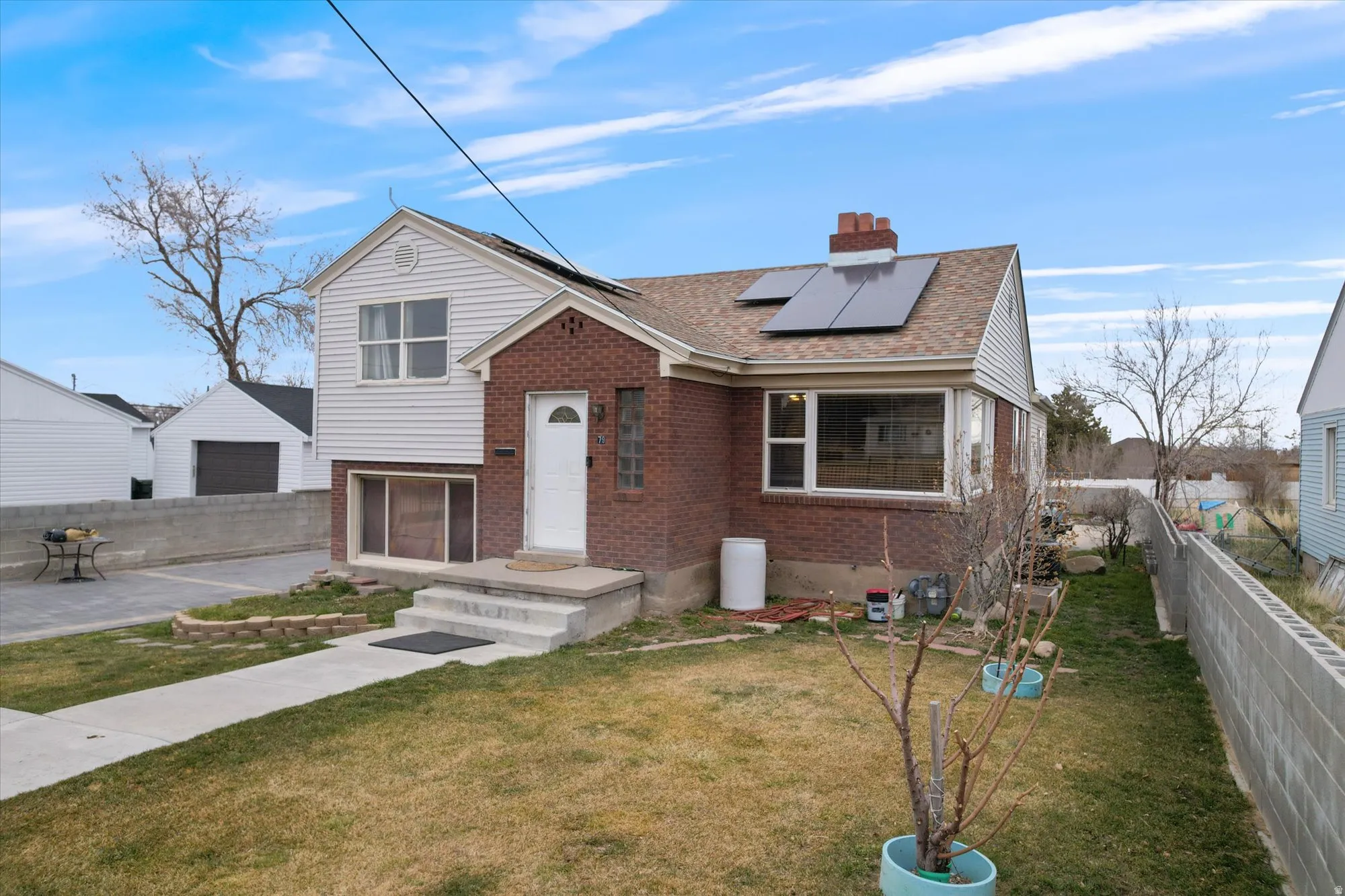 View of front facade with solar panels, brick siding, a chimney, and roof with shingles