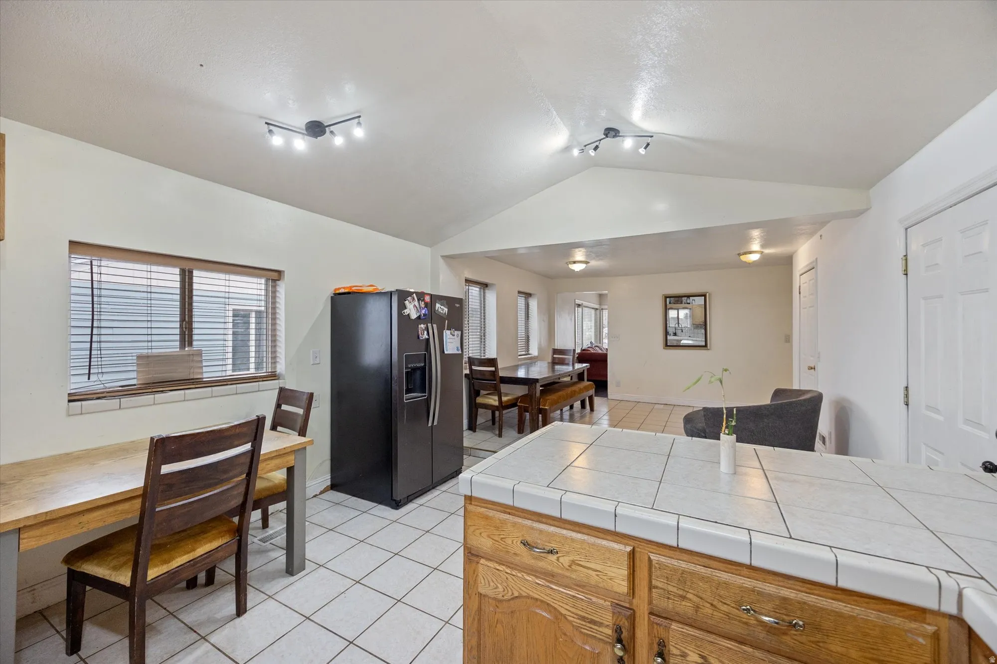 Kitchen with fridge with ice dispenser, light tile patterned floors, tile counters, wood finish cabinetry, and rail lighting