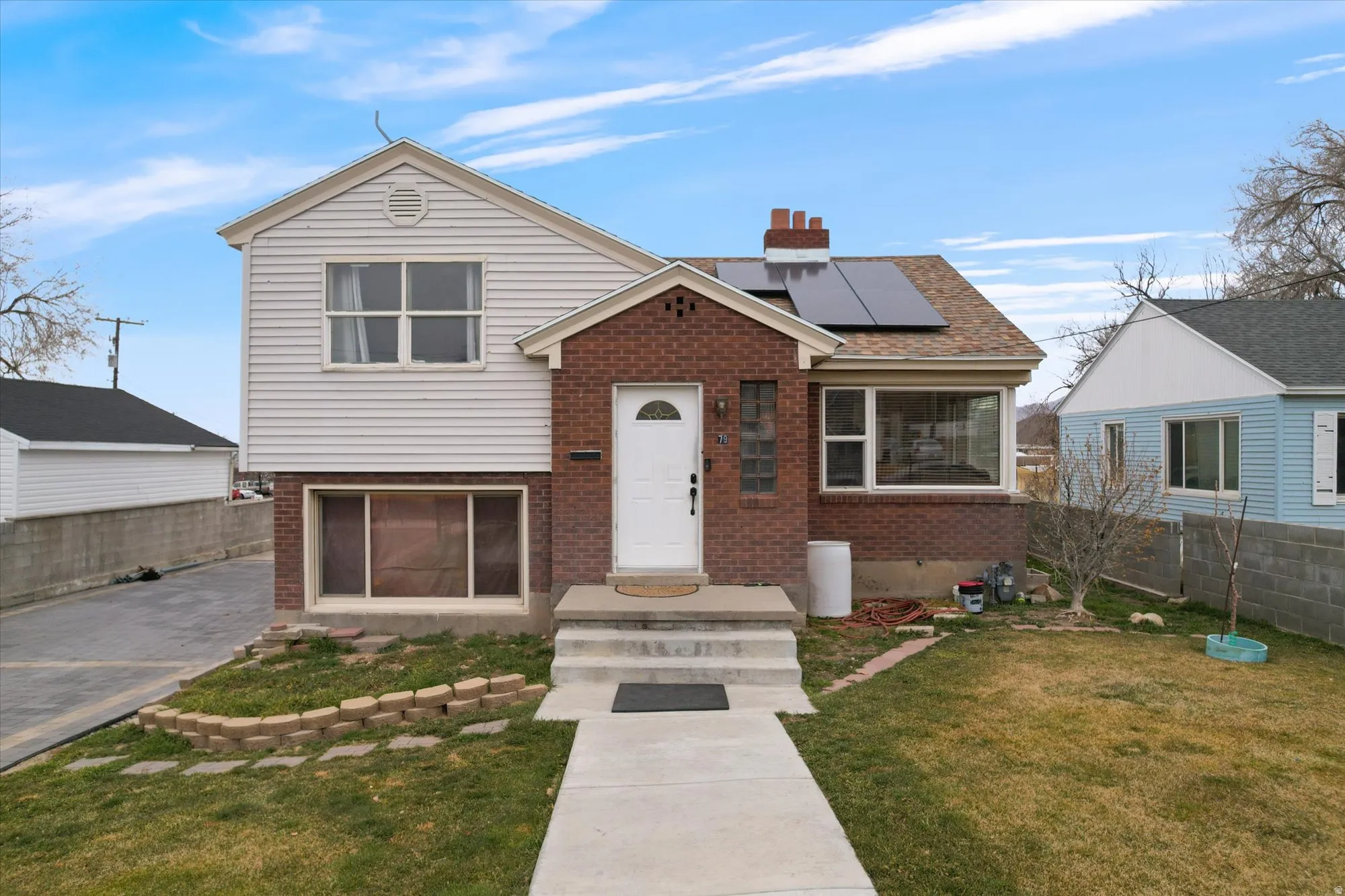 Tri-level home featuring solar panels, brick siding, and a chimney