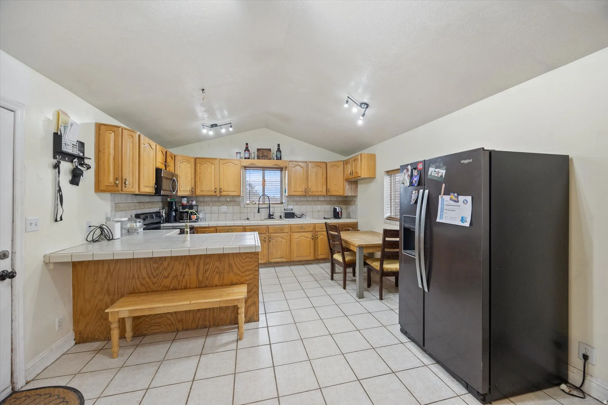 Kitchen featuring tile counters, black fridge, a peninsula, tasteful backsplash, and light tile patterned floors