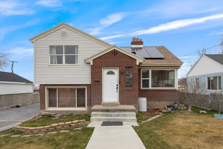 View of front of property with solar panels, brick siding, and a chimney
