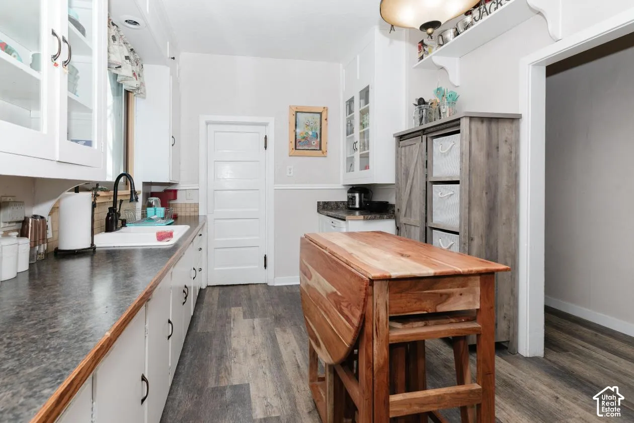 Kitchen with white cabinetry, glass fronted cabinets, dark countertops, and dark wood-style floors
