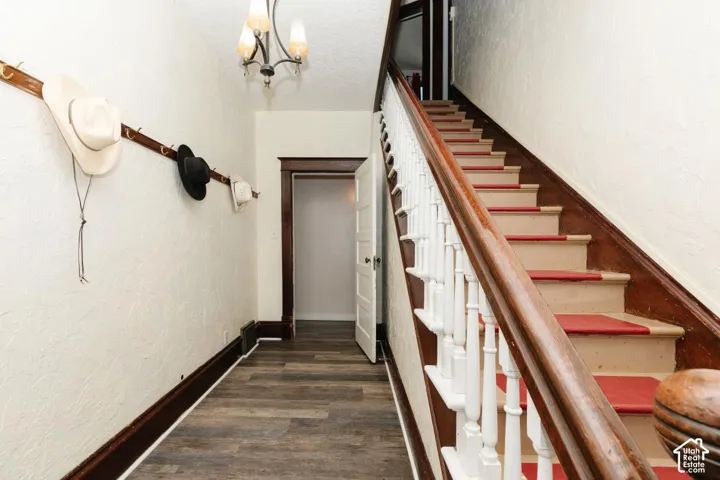 Stairs with a textured wall, wood finished floors, and suspended lighting
