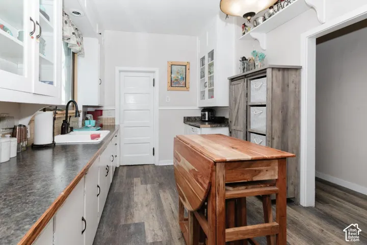 Kitchen with white cabinetry, glass fronted cabinets, dark countertops, and dark wood-style floors