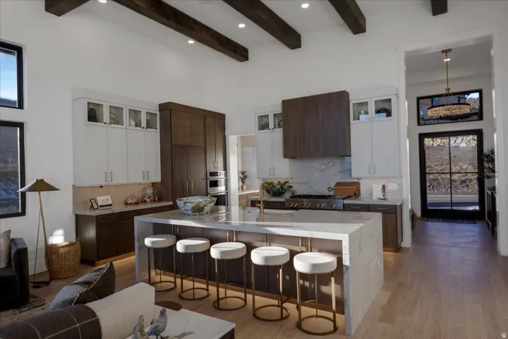 Kitchen featuring dual tone cabinets, glass fronted cabinets, a kitchen breakfast bar, light wood-type flooring, and light stone counters