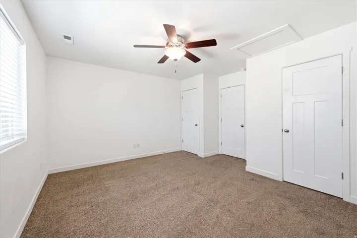 Spacious room featuring carpeting, a ceiling fan with integrated lighting, multiple paneled doors, and a window with blinds