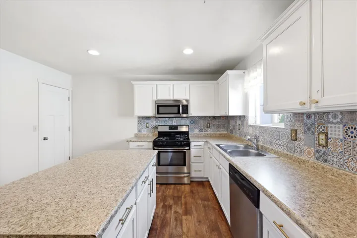 Kitchen featuring an island with ample countertop space, white cabinetry, stainless steel appliances, a double basin sink, and a decorative tile backsplash