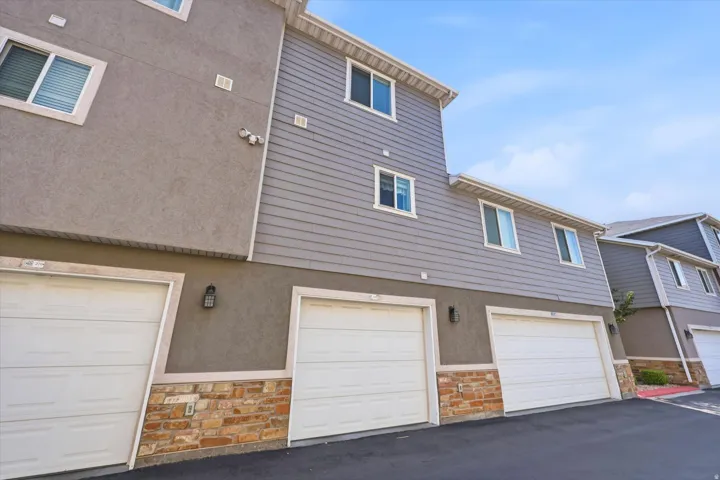 Townhome exterior featuring gray stucco, horizontal siding, white-trimmed windows, and attached garages