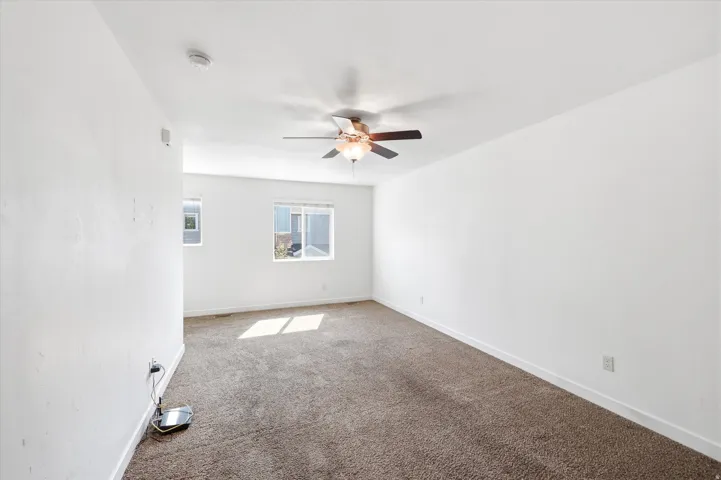 Carpeted room featuring multiple windows, a ceiling fan with integrated lighting, and white walls