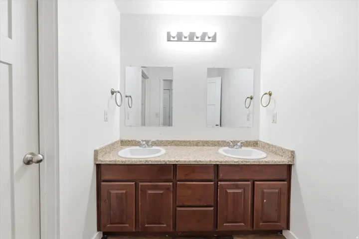 Dual vanity with wood-finish cabinetry, granite-style countertop, and individual mirrors