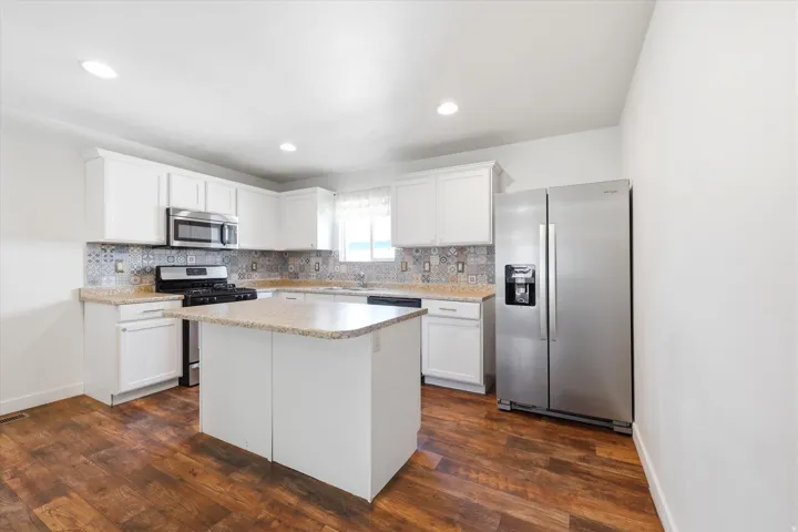 Kitchen featuring white cabinetry, patterned tile backsplash, wood-finish flooring, recessed lighting, and stainless steel appliances