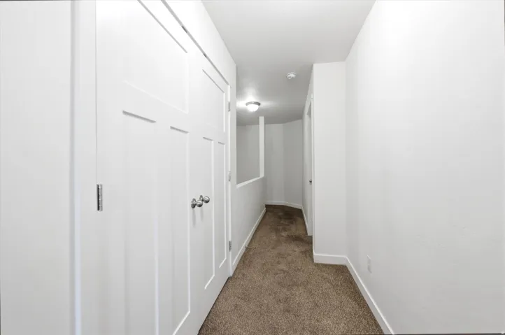 Hallway featuring neutral carpet flooring, crisp white walls, recessed lighting, and white paneled doors with brushed nickel hardware