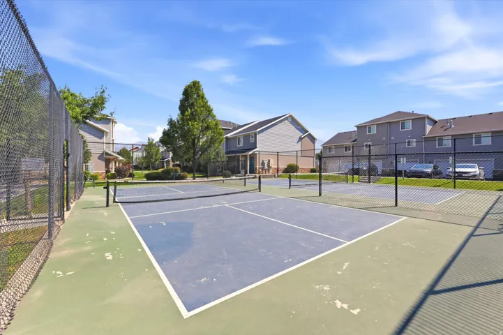 Dual tennis courts with chain-link fencing, surrounded by mature trees and residential structures