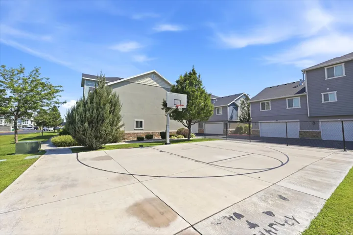 Paved basketball court with a hoop, surrounded by green lawns and mature trees